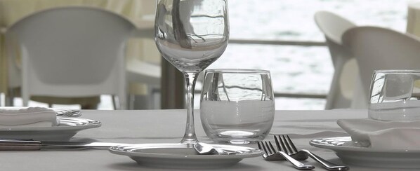 Una mesa servida con platos blancos, una copa de vino, un vaso de agua y cubiertos.