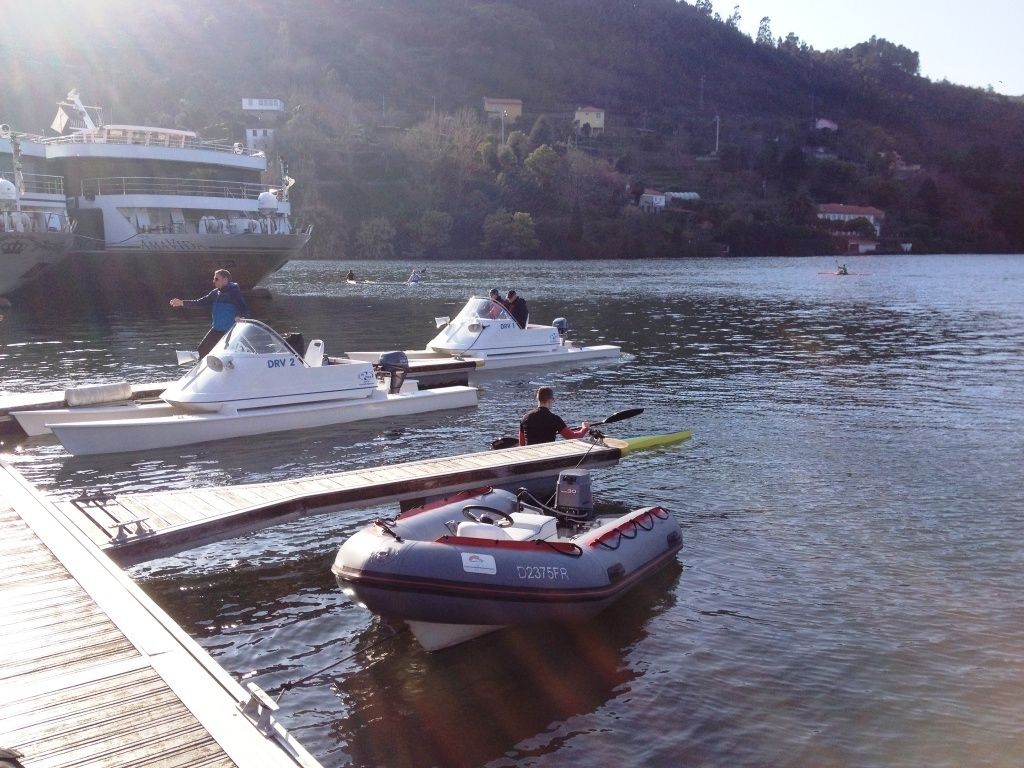 A marina with several boats docked, a dock, and a hilly landscape in the background.