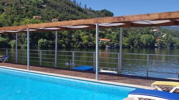 A pool area with lounge chairs and a wooden deck overlooking a lake.