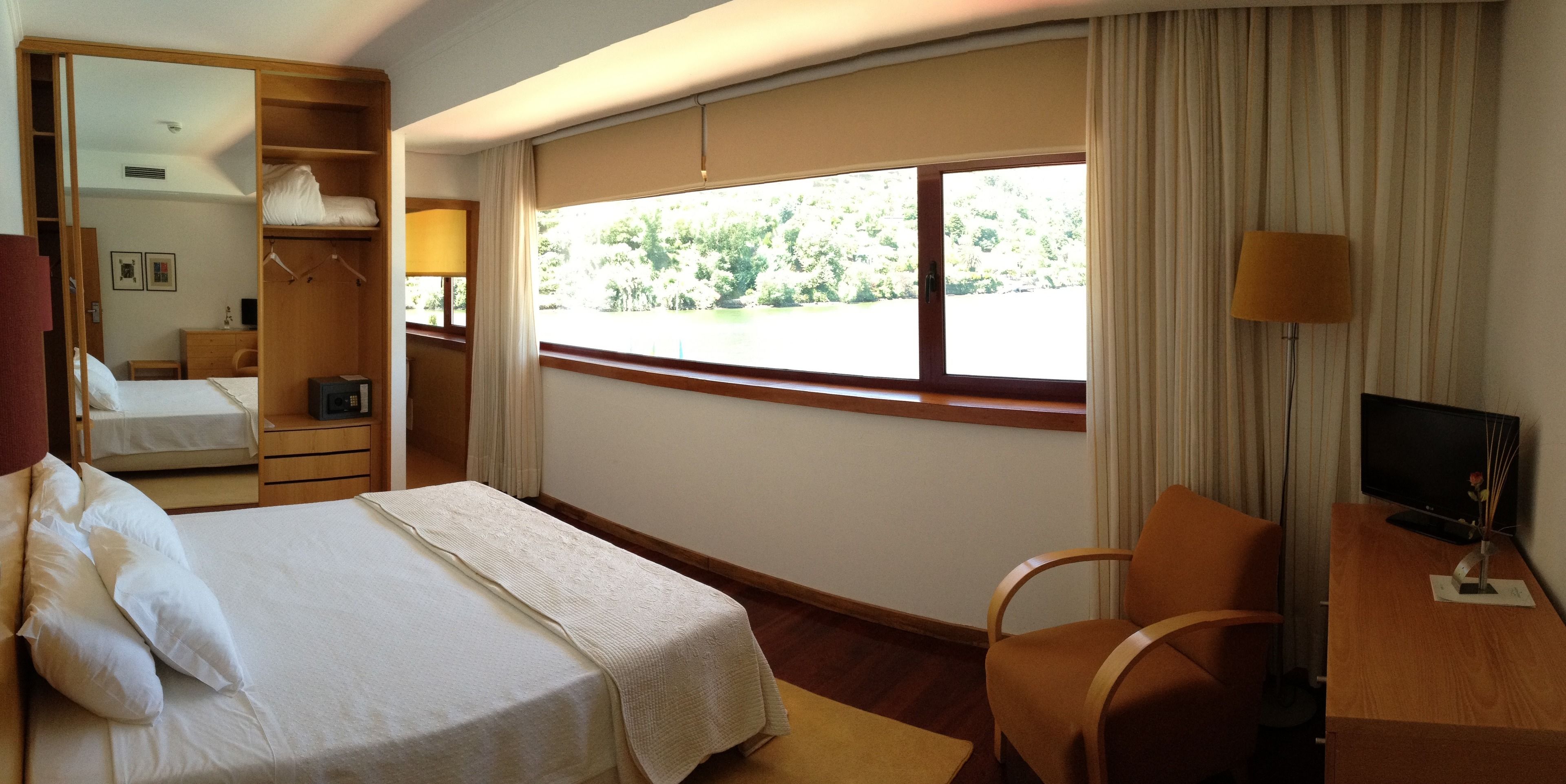 Habitación de hotel con cama, escritorio con televisor, silla, ventana con cortinas y armario.