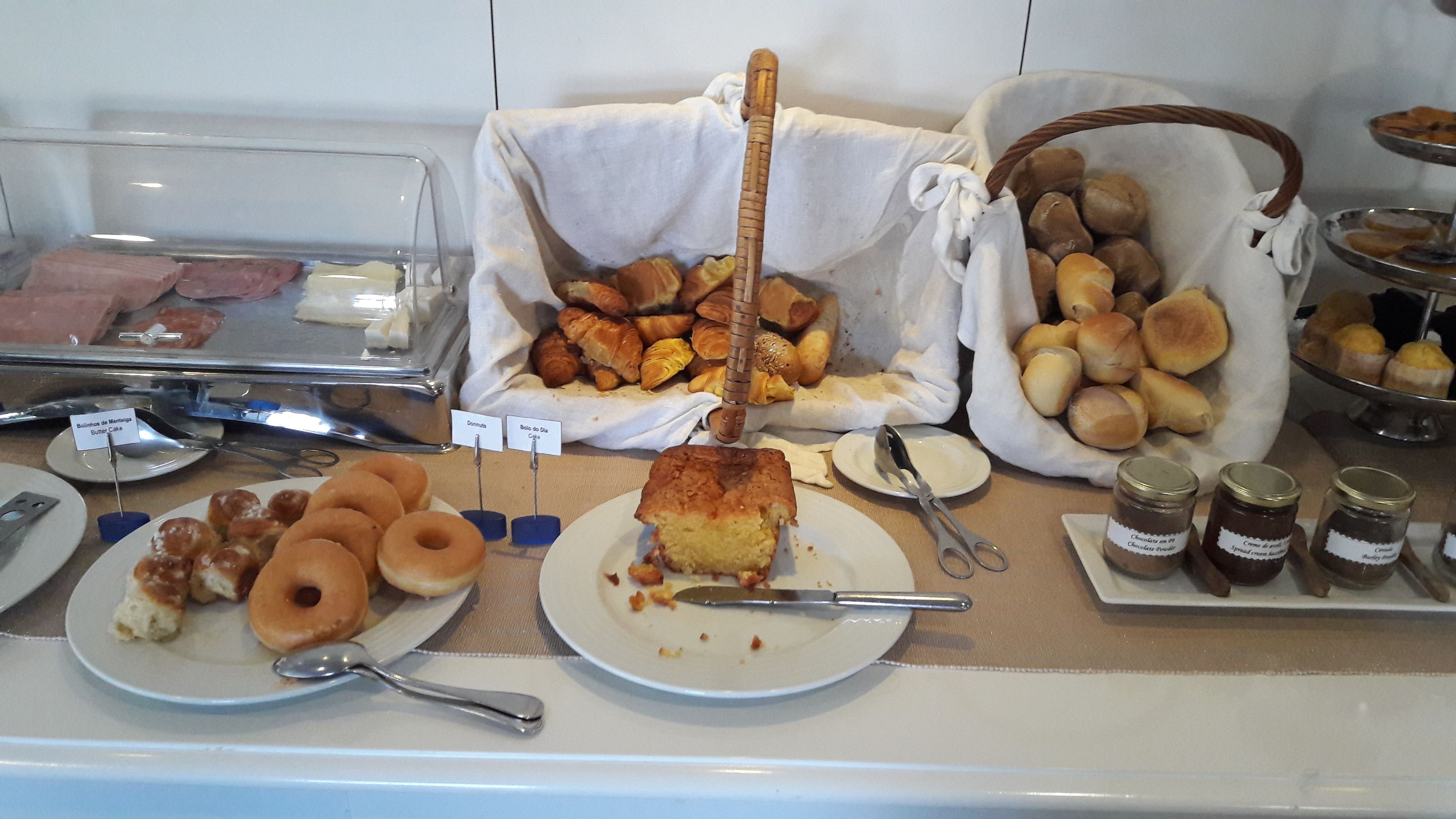 Un buffet proposant une variété de produits de boulangerie, notamment des pâtisseries et du pain, ainsi que des accompagnements comme de la pâte à tartiner au chocolat et du beurre.