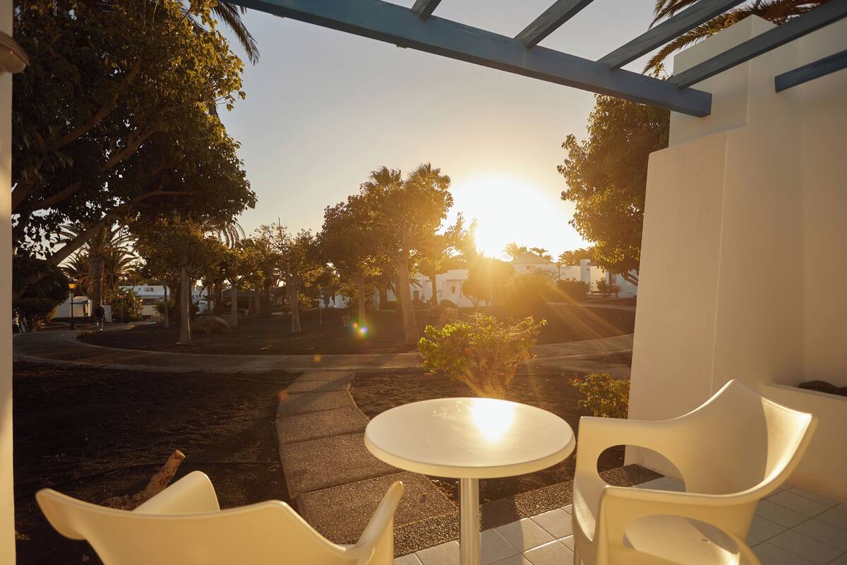 Un área de estar al aire libre con una mesa y sillas, rodeada de árboles y vista al atardecer.