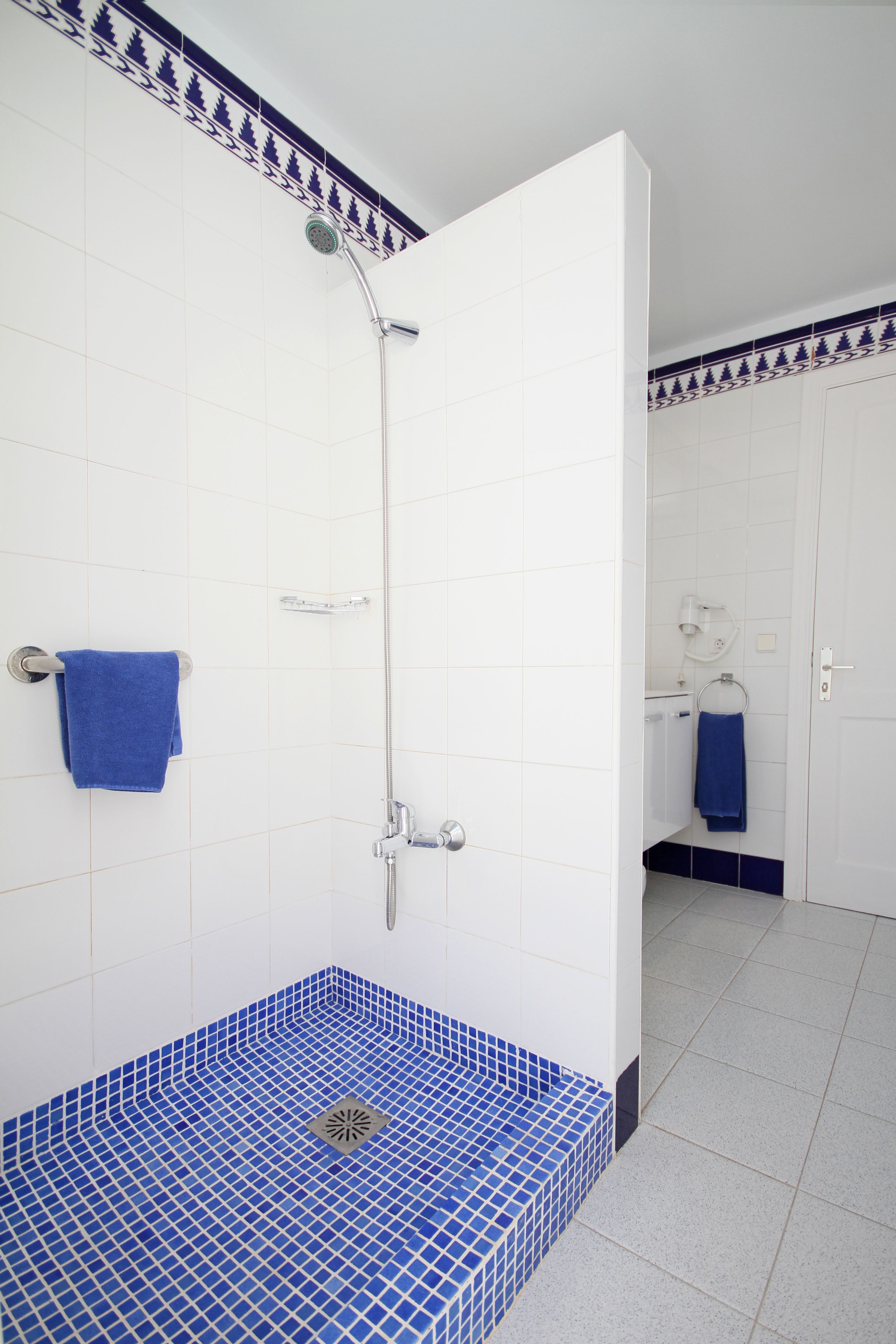 A bathroom with a shower, white tiled walls, and a blue-tiled floor.