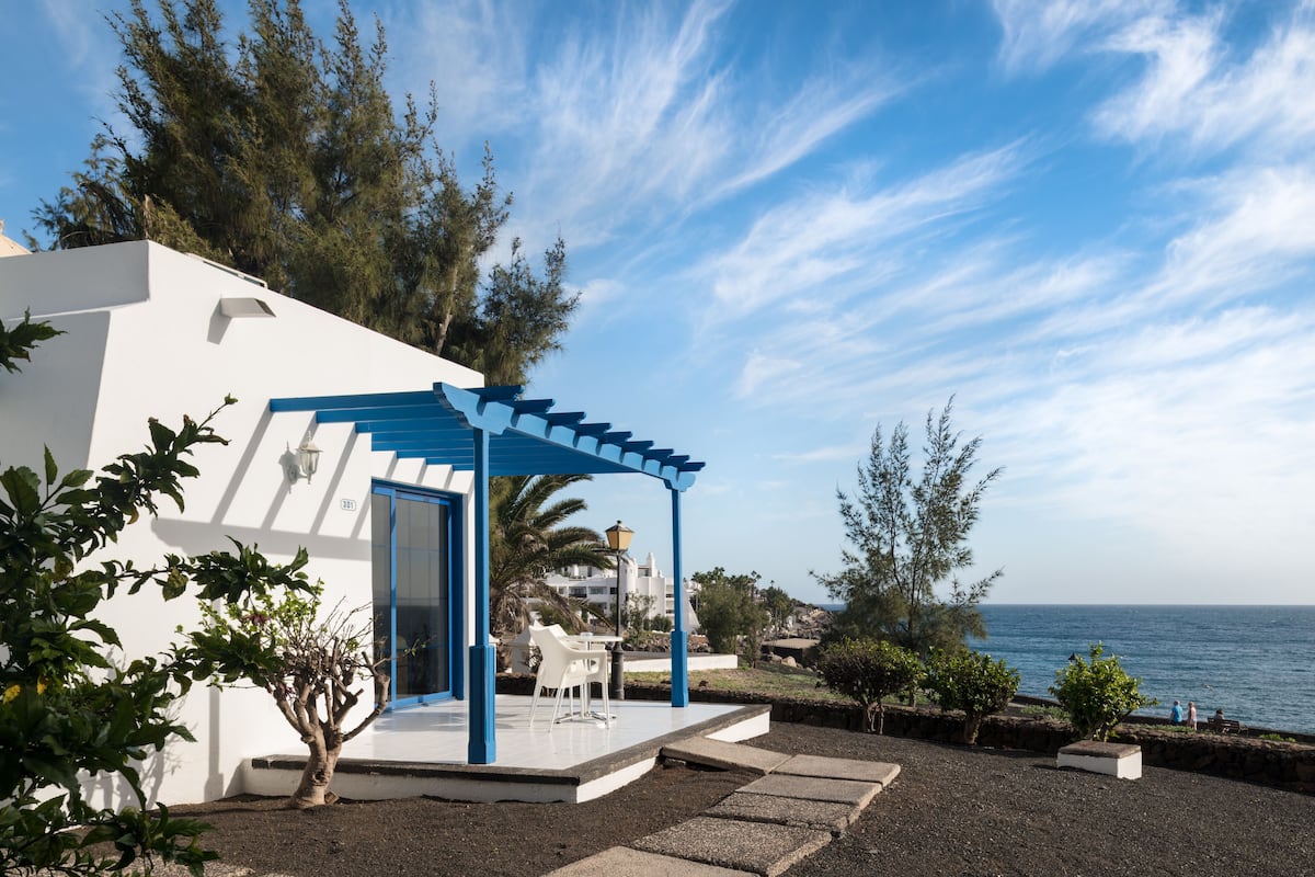 Un edificio blanco con puerta azul y un patio cubierto con mesa y sillas.