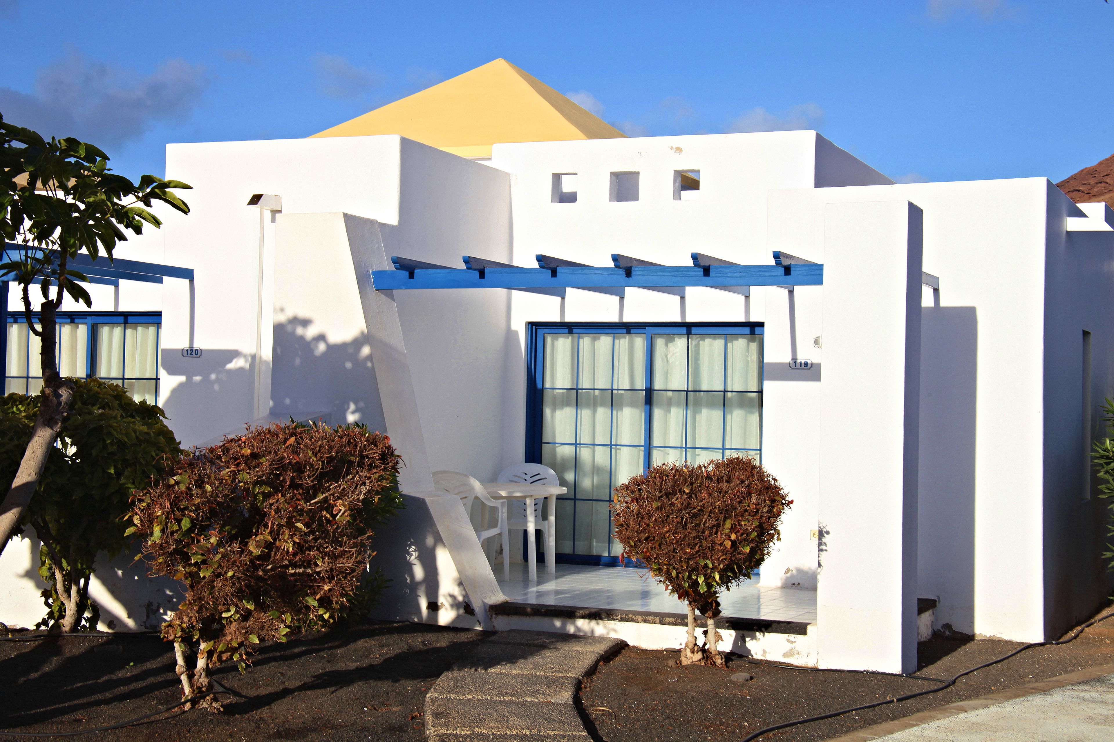 A modern building with a white exterior, blue accents, and a small patio area with a table and chairs.