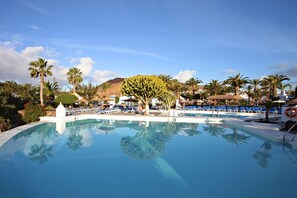 Una piscina con agua cristalina y azul, rodeada de palmeras y sillas de descanso.