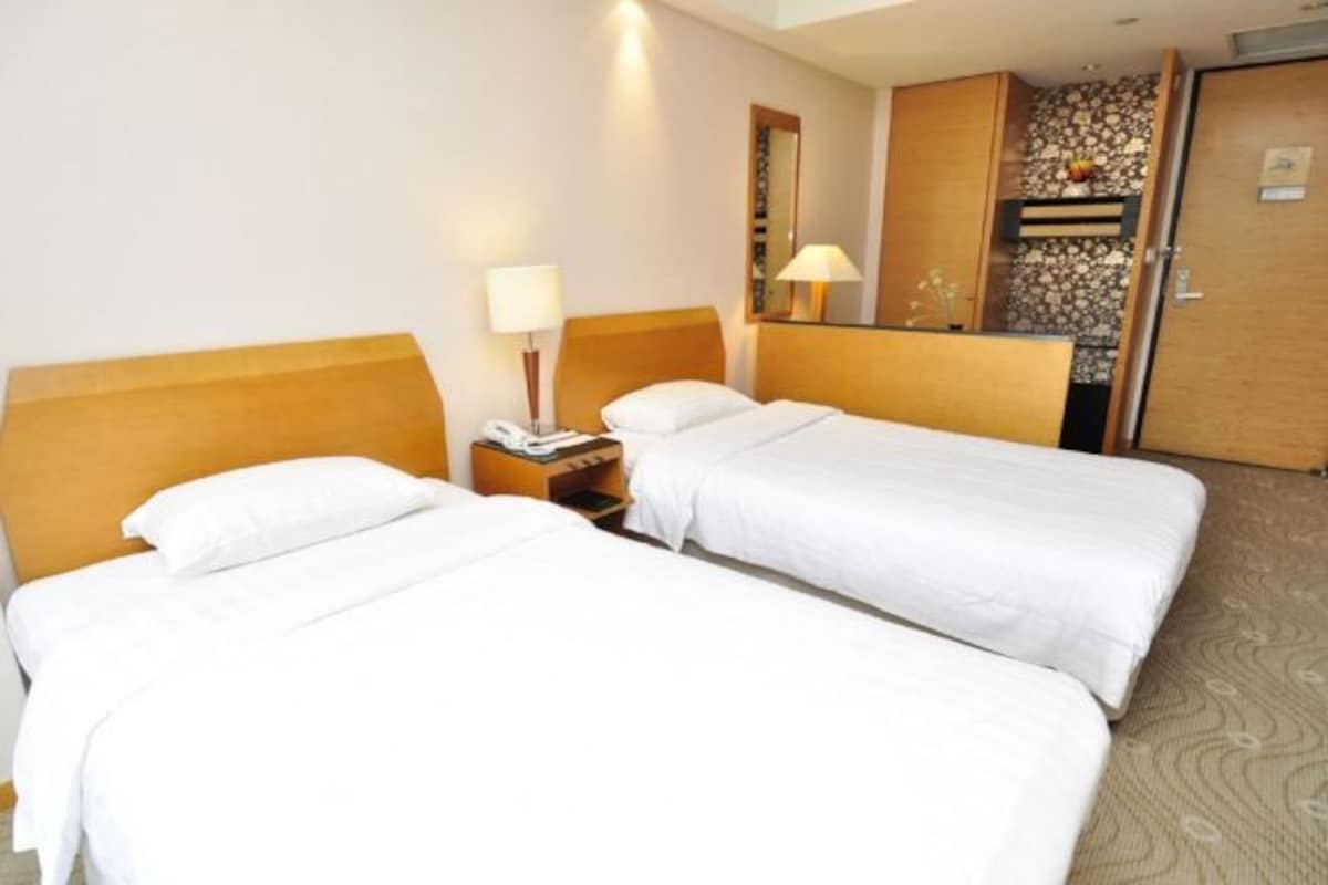 A hotel room with two single beds, a bedside table with a lamp, a phone, and a mirror.