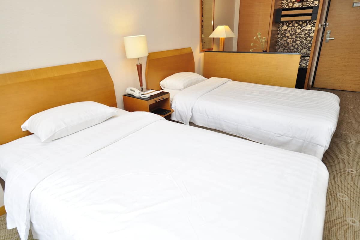 Quarto de hotel com duas camas de solteiro, mesa de cabeceira com abajur e espelho sobre a cama.