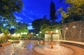 Un espace extérieur aménagé pour la nuit, avec un élément aquatique, des murs en pierre et des plantes en pot.