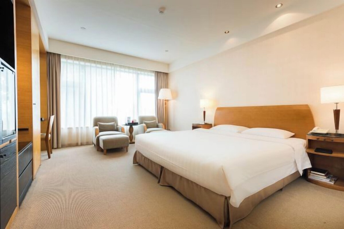 A hotel room with a large bed, a desk, a chair, and a television.