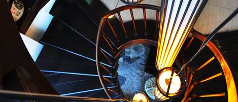 Una escalera de caracol con barandilla de metal e iluminada por lámparas verticales.