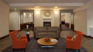 A lobby with a fireplace, two orange armchairs, a coffee table, and a patterned carpet. - Homewood Suites by Hilton San Antonio North (San Antonio)
