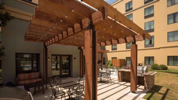 An outdoor patio area with wooden pergola, seating, and a barbecue setup. - Homewood Suites by Hilton San Antonio North (San Antonio)