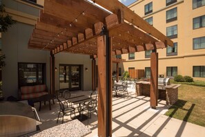 Un patio al aire libre con pérgola de madera, mobiliario y zona de barbacoa.