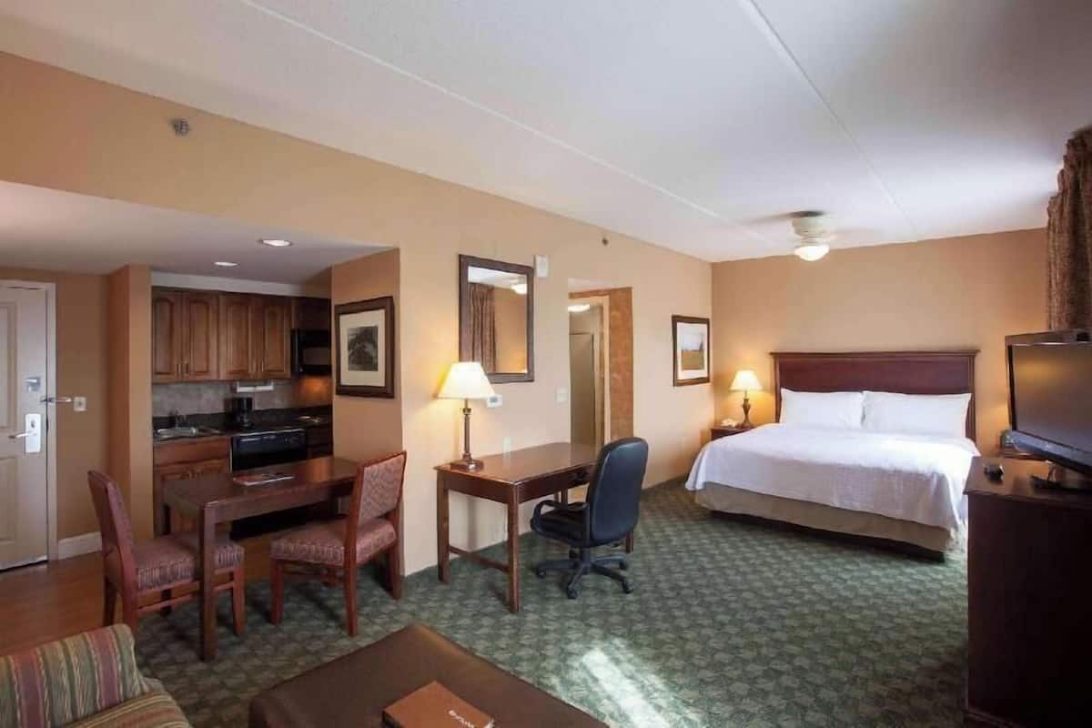 Ein Hotelzimmer mit Bett, Schreibtisch, Stuhl, Küchenzeile und Fernseher.