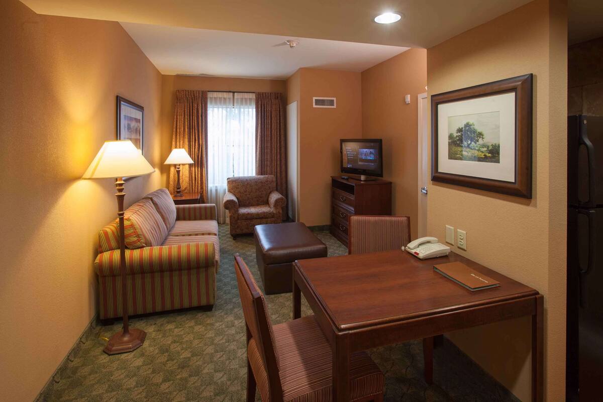 Ein Hotelzimmer mit einer Couch, einem Sessel, einem Esstisch und einem Fernseher.