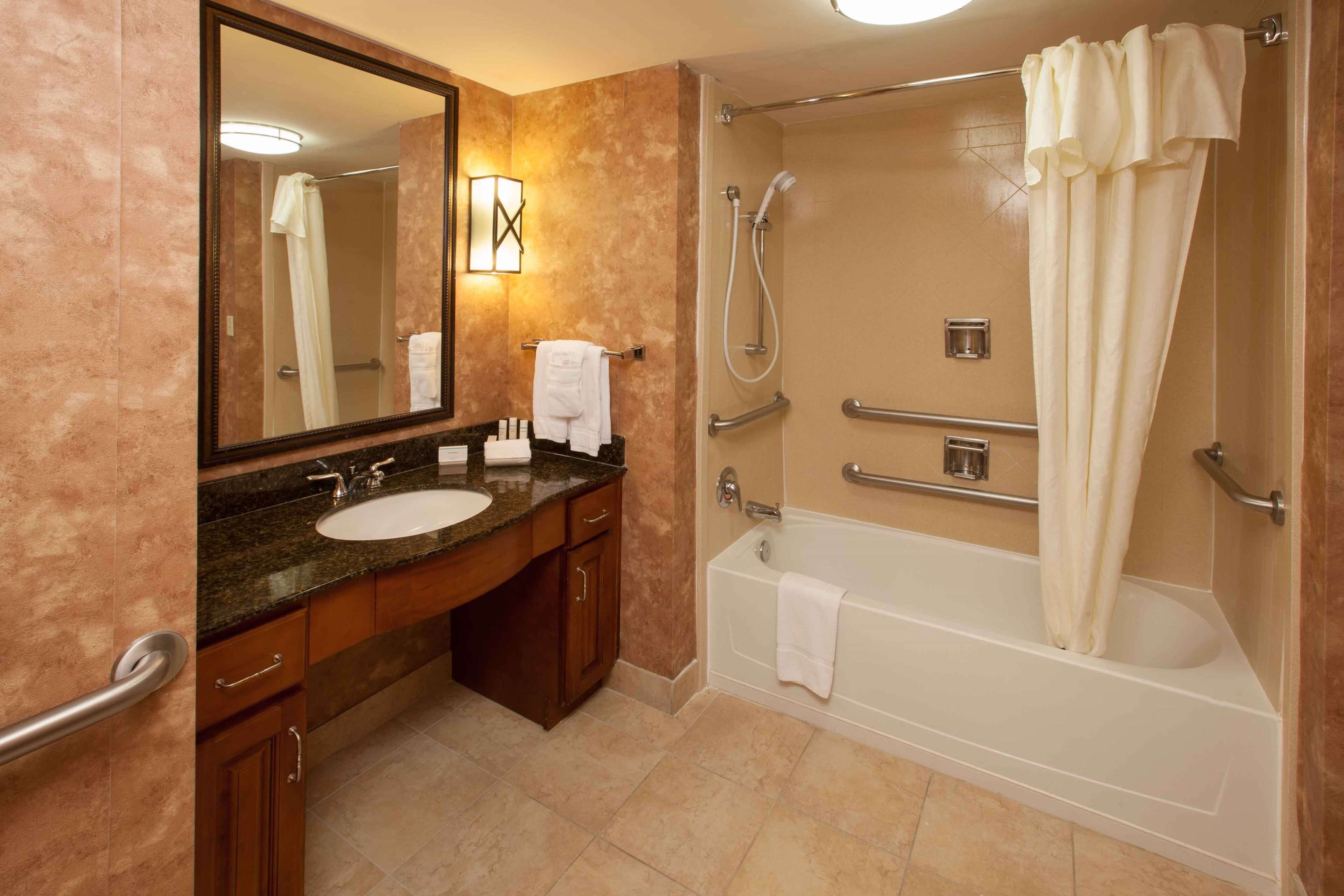 A bathroom with a sink, mirror, vanity, and a walk-in shower with grab bars.