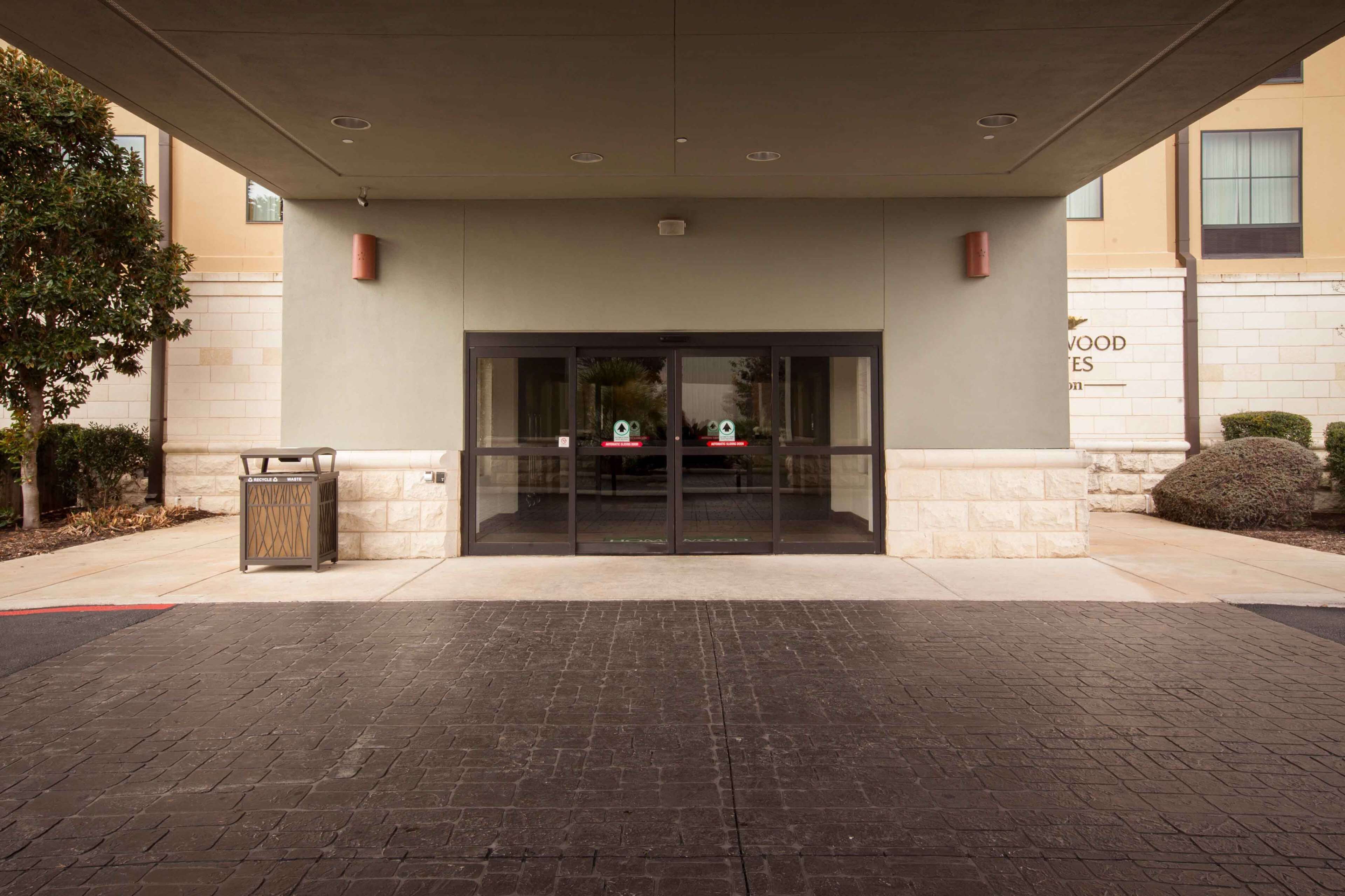 A building entrance with a glass door, a trash bin, and a paved walkway.