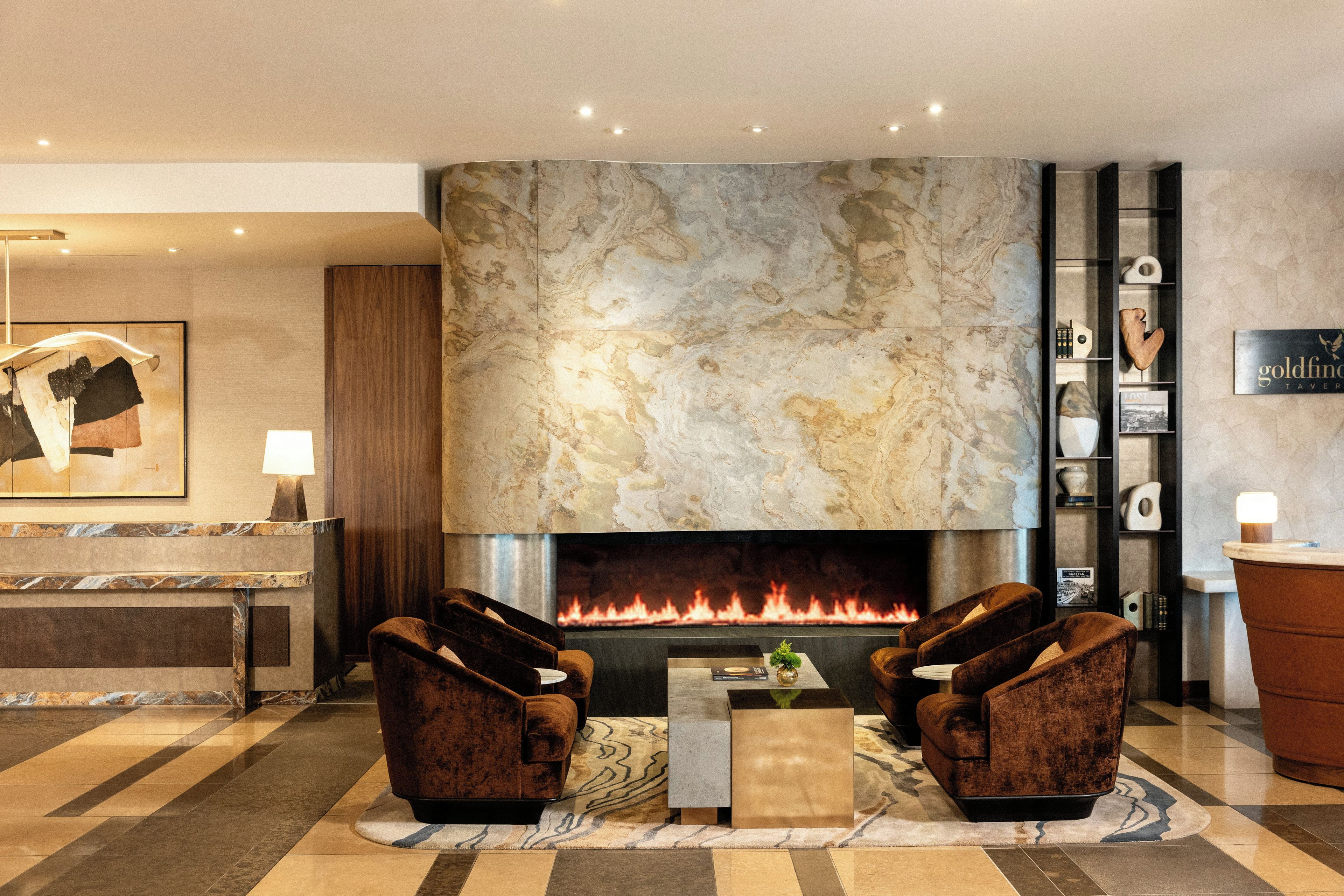 A lobby with a fireplace, two armchairs, a reception desk, and a sign for 'Goldfinch Tavern'.