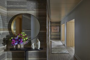 A hallway with a round mirror on a wall, a vase with flowers, and a wooden floor.