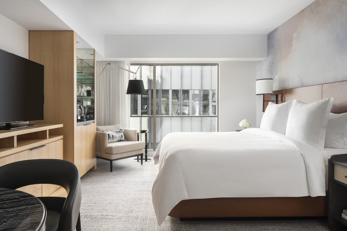 A hotel room with a large bed, a TV, a desk, and a chair.