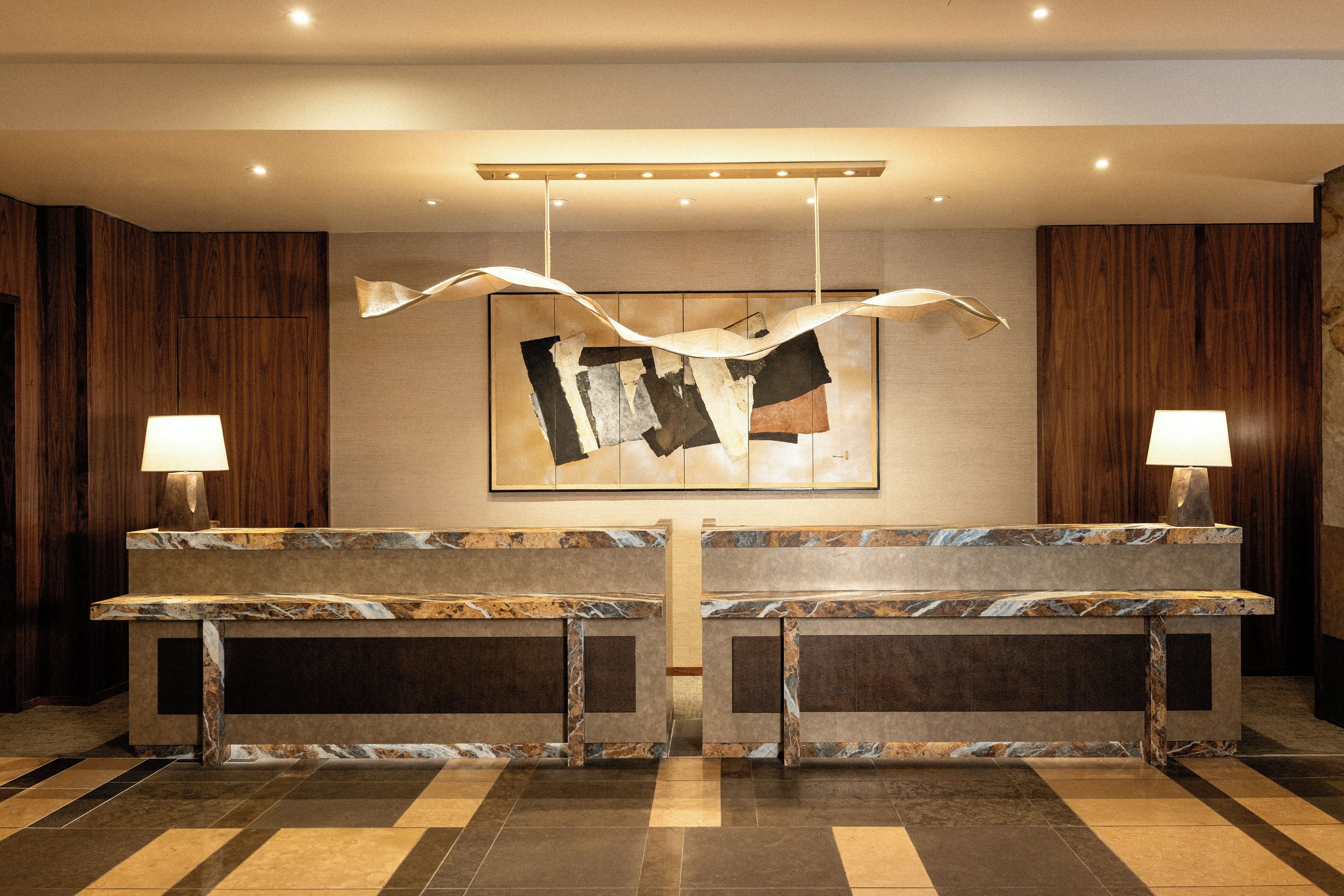 A reception desk with two lamps, a hanging abstract artwork, and a patterned floor.