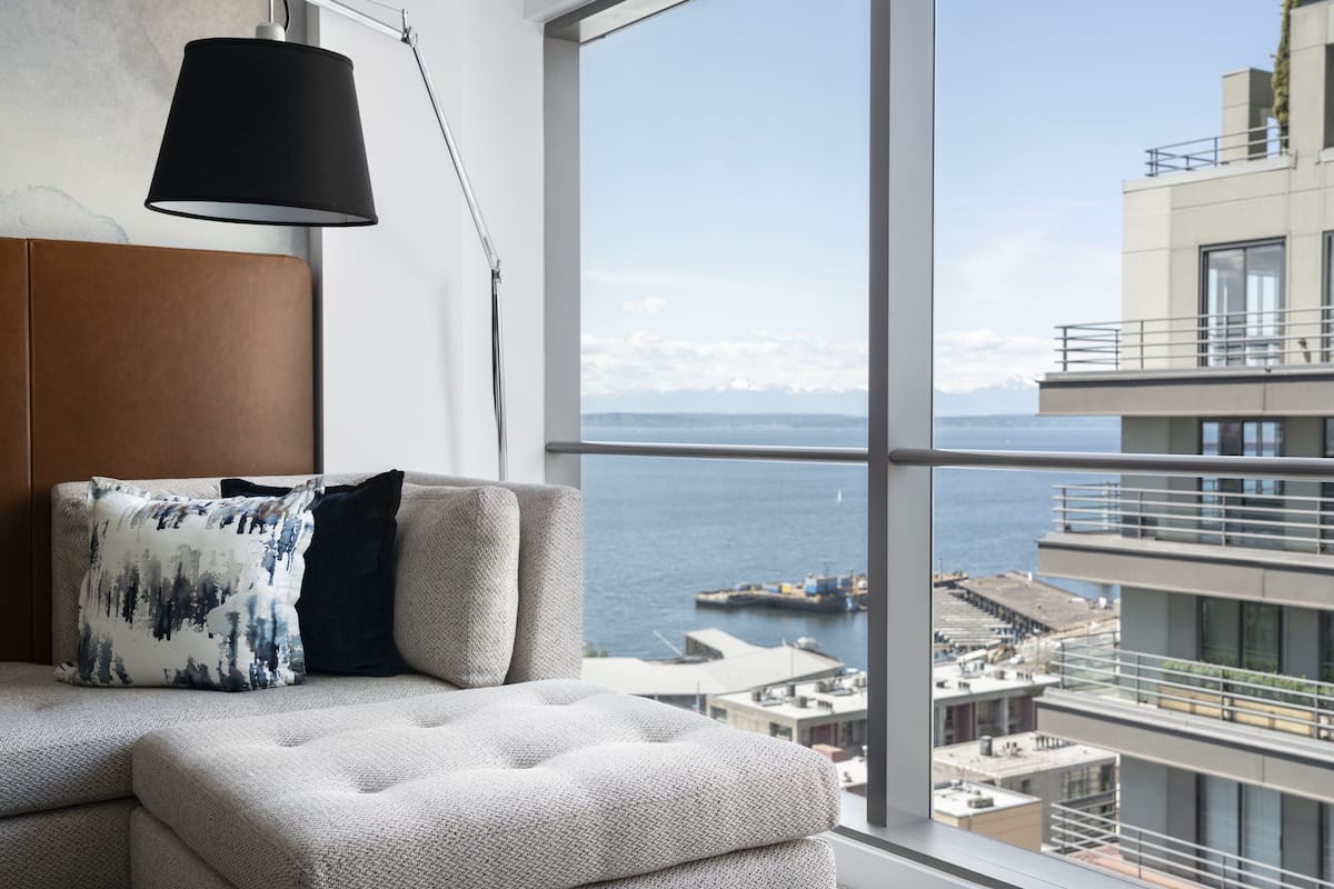 A modern living room with a large window, a sofa, and a lamp.