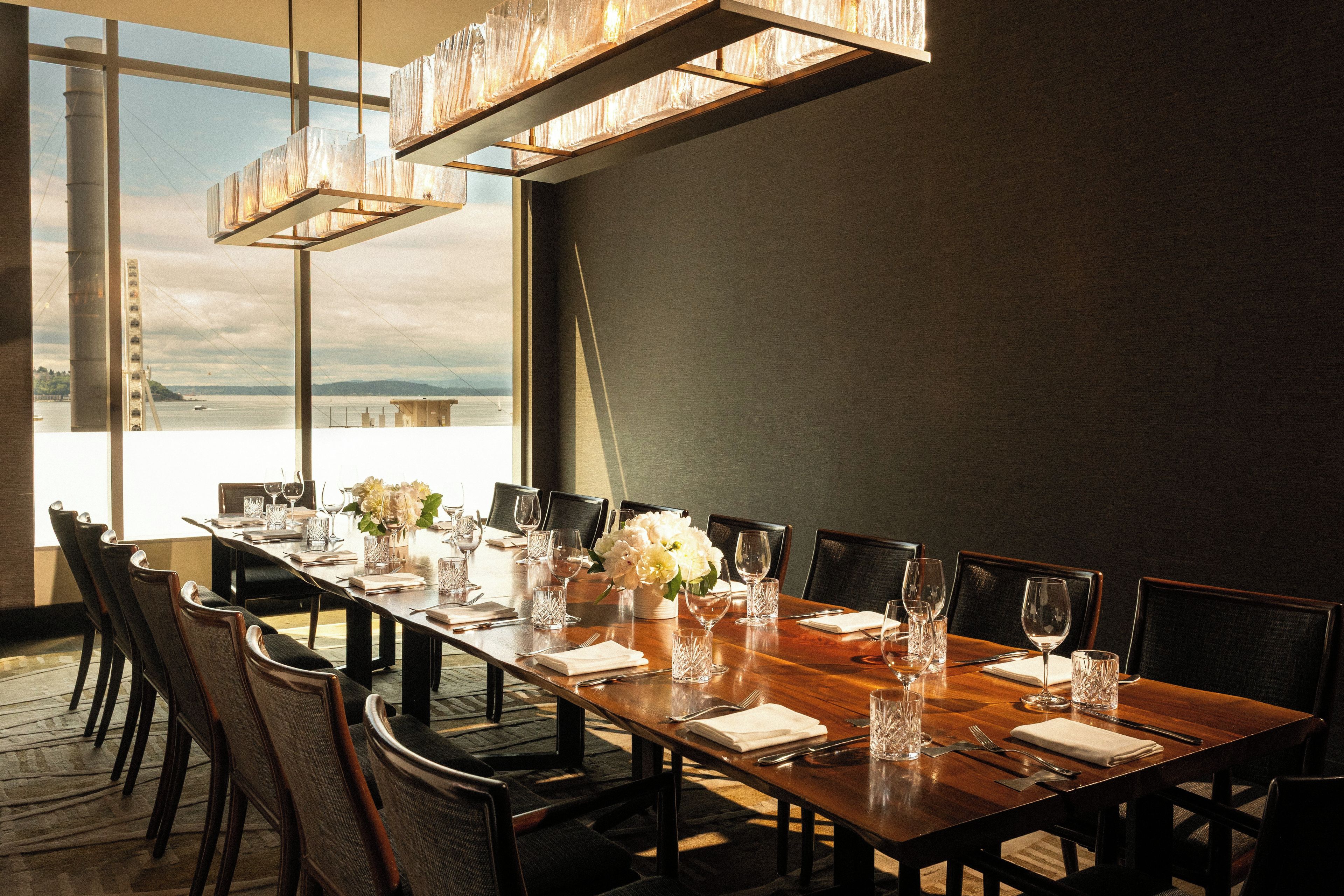 A dining area with a long table set for a meal, chairs, and a view of the water.
