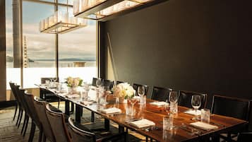 A dining area with a long table set for a meal, chairs, and a view of the water.