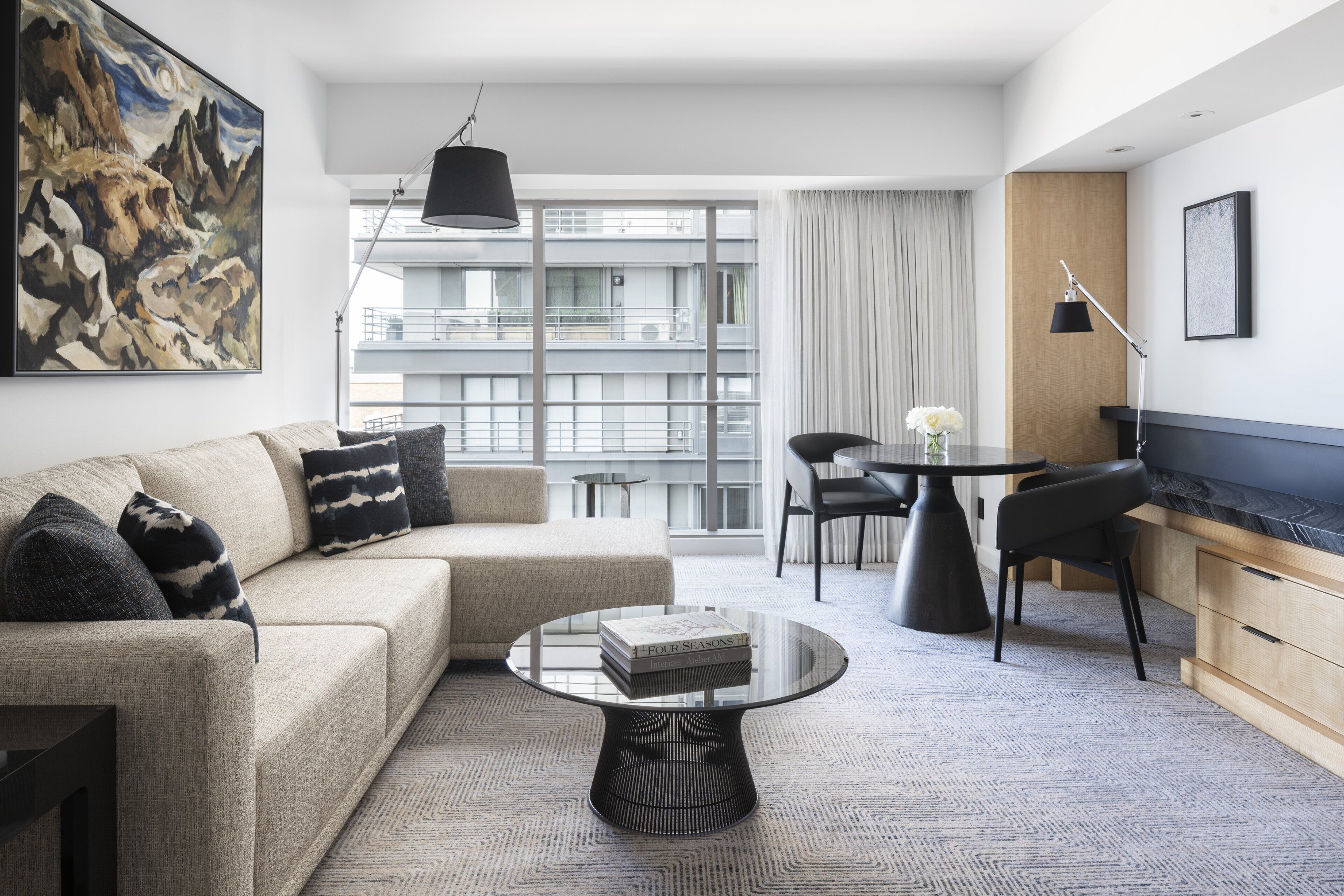 Una habitación de hotel moderna con sofá, una mesita de centro, una mesa de comedor con sillas, televisión y un ventanal con vistas a la ciudad.