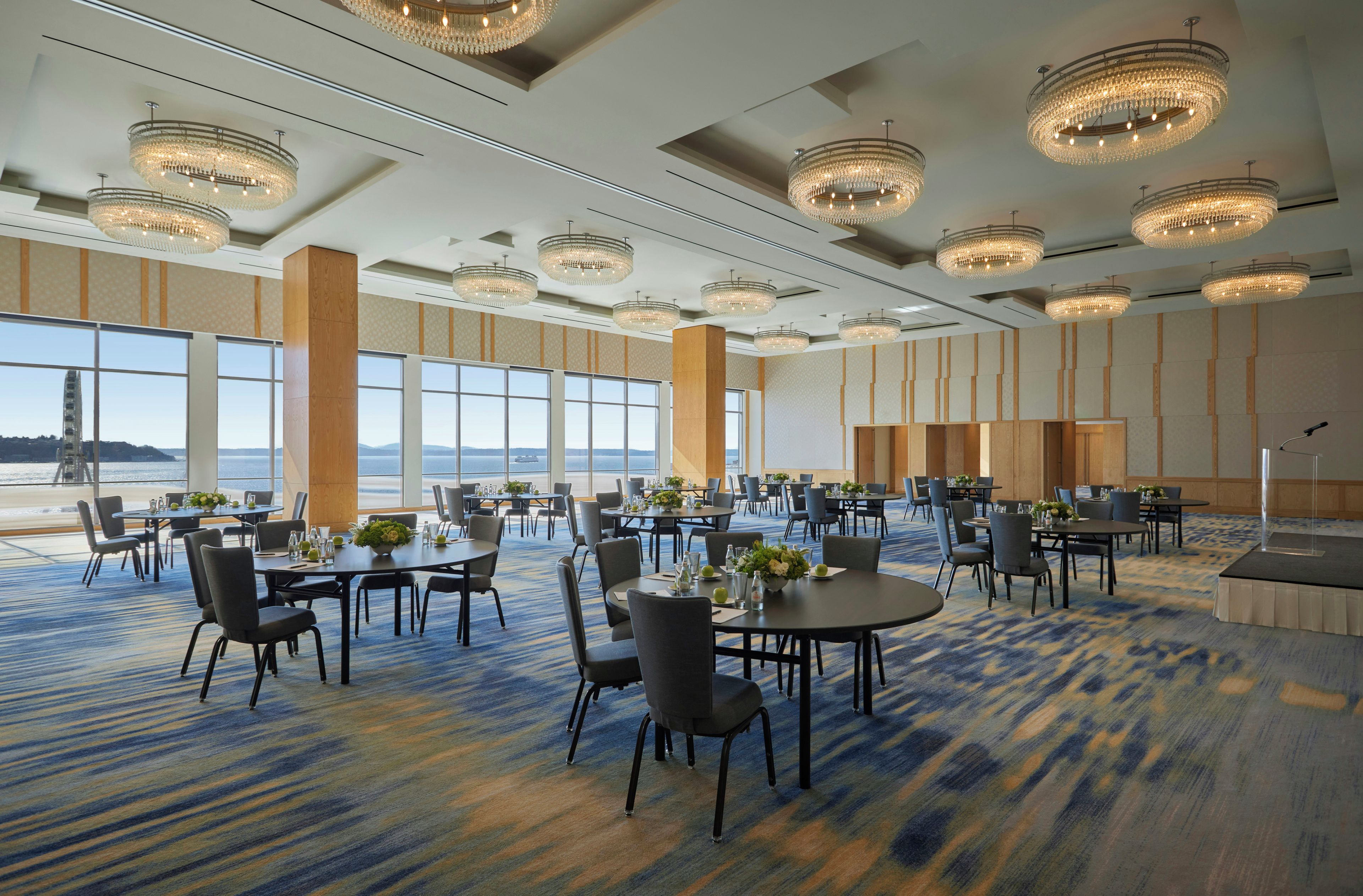 A spacious conference room with multiple tables and chairs, large windows offering a view, and ornate chandeliers.
