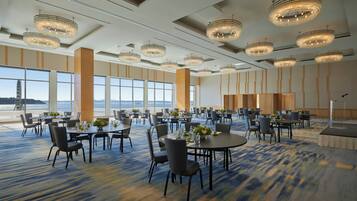 A spacious conference room with multiple tables and chairs, large windows offering a view, and ornate chandeliers.