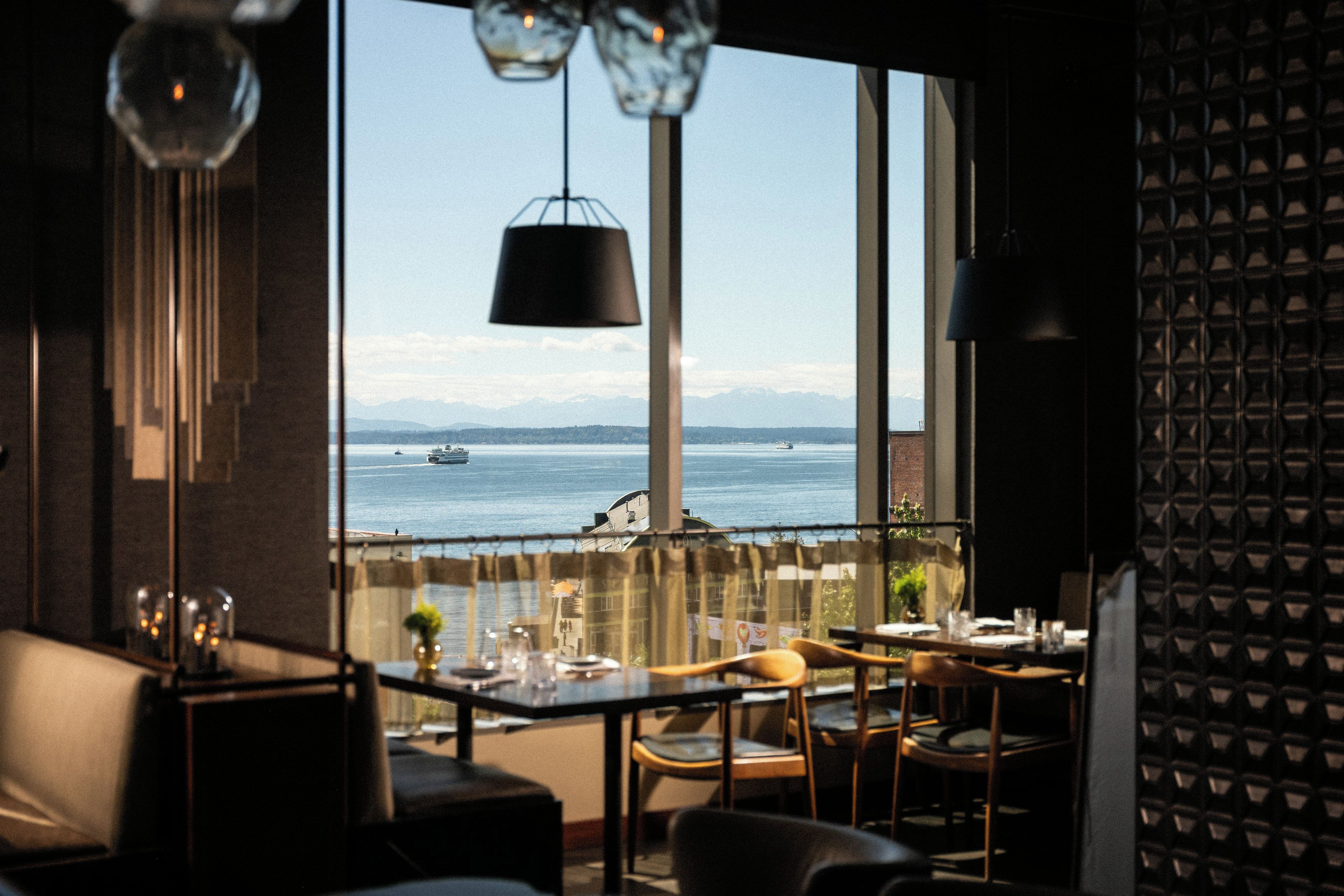 A dining area with a view of the sea and mountains through large windows.