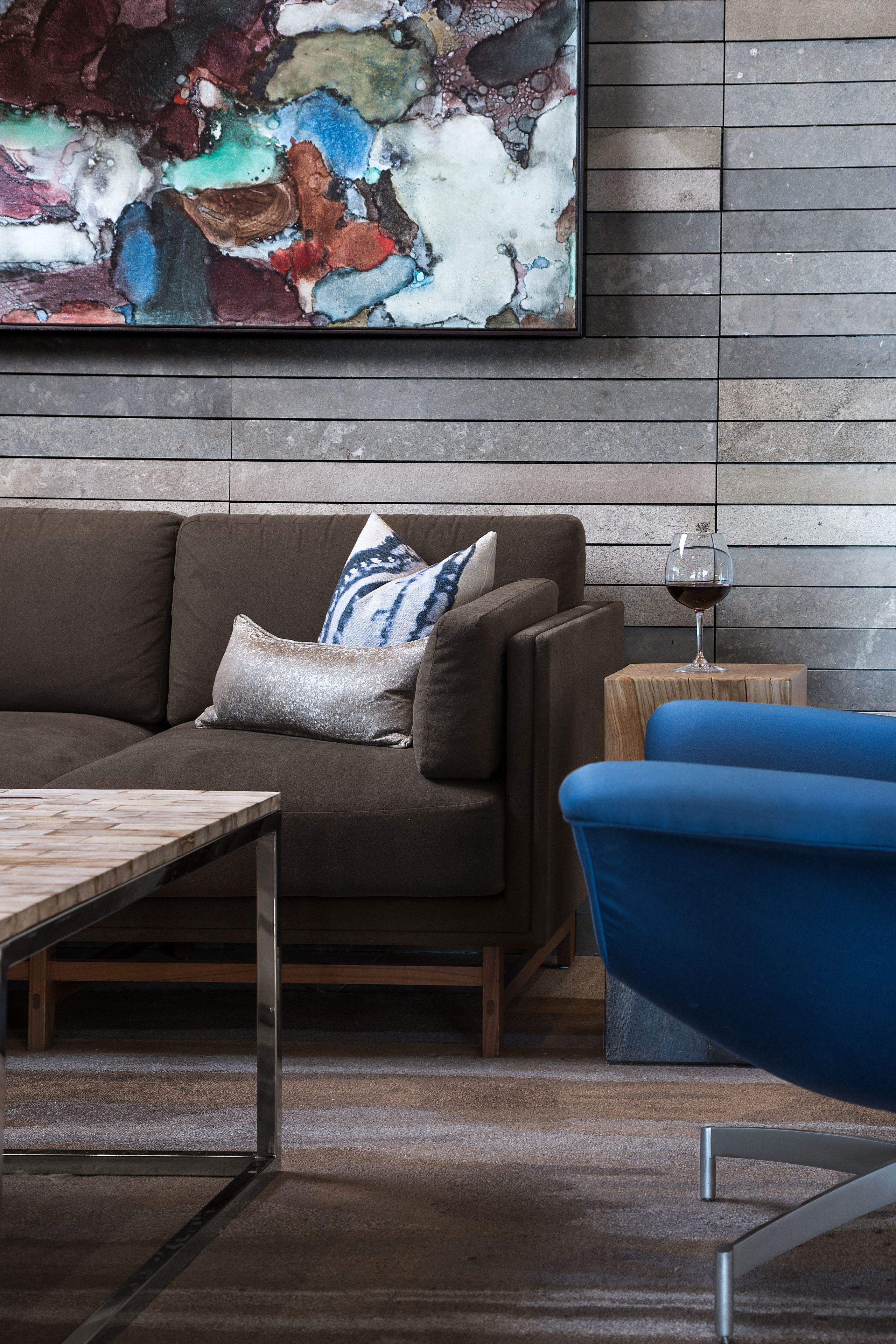 Uma sala de estar moderna com um sofá marrom, uma poltrona azul, uma mesa de centro de madeira e uma taça de vinho sobre uma mesa lateral de madeira.