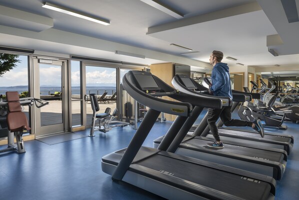 Un gimnasio con cintas de correr, equipo de ejercicio y grandes ventanales que ofrecen vistas al exterior.