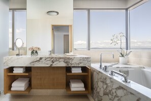 A modern bathroom with a marble vanity, a large window, and a view of the ocean.