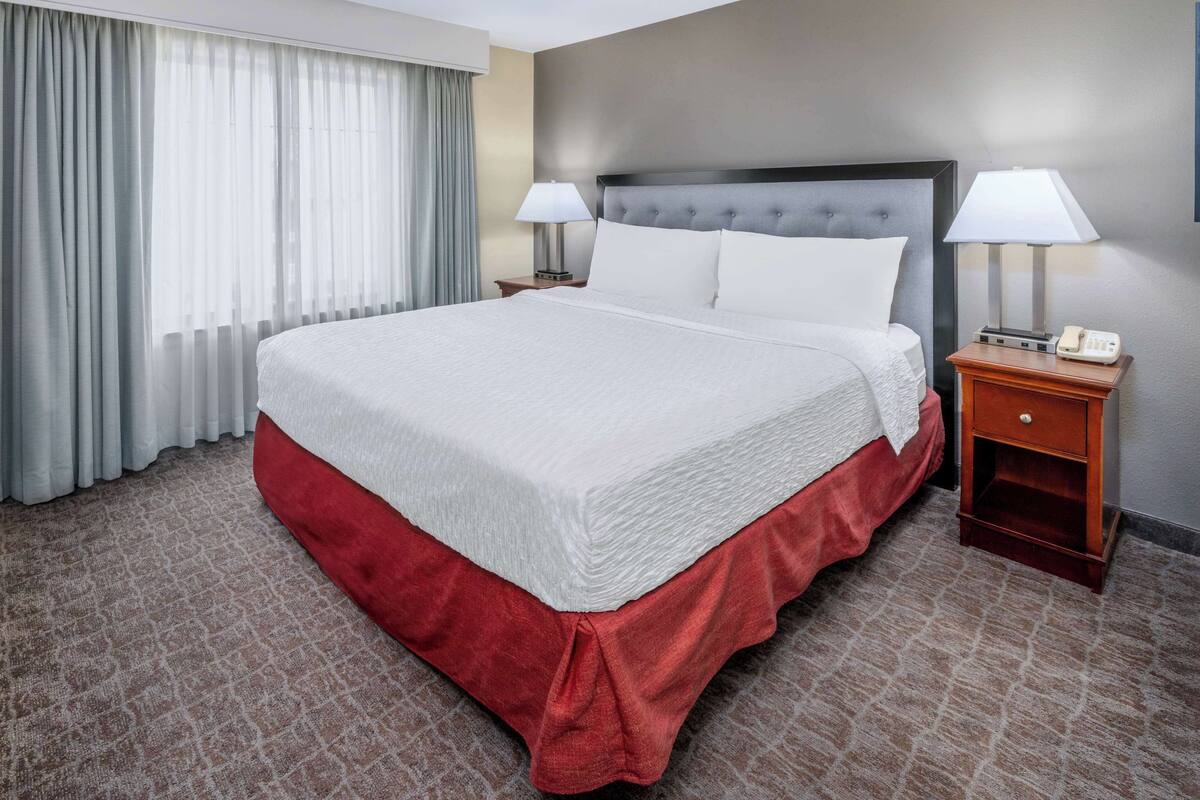 Une chambre d’hôtel avec un grand lit, deux tables de chevet avec des lampes, un couvre-lit rouge et une moquette à motifs.