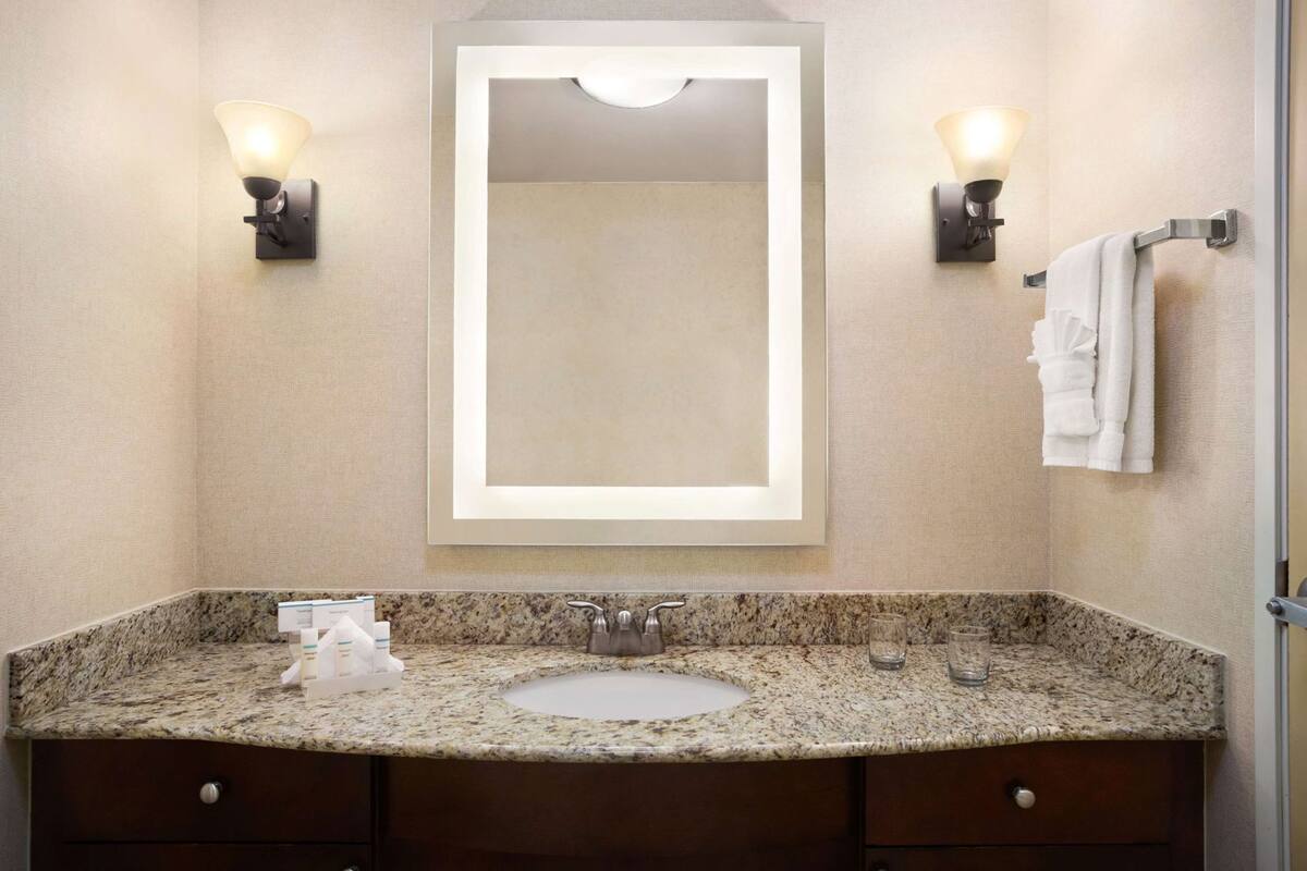 A bathroom with a granite countertop, a sink, a mirror, and two wall-mounted light fixtures.