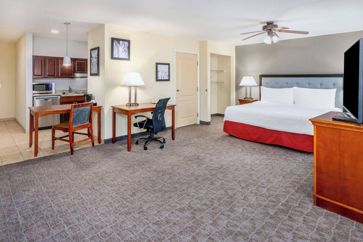Une chambre d’hôtel équipée d’un lit, d’un bureau, d’une chaise, d’une kitchenette et d’un ventilateur de plafond.