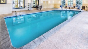 Ein großer, überdachter Schwimmbereich mit klarem, blauem Wasser, umgeben von gefliestem Boden und ausgestattet mit Liegestühlen und einem Tisch.
