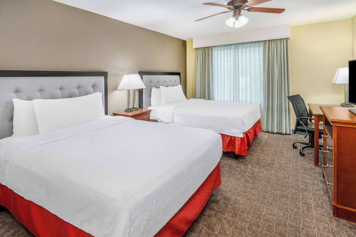 Une chambre d’hôtel avec deux lits, un bureau, une chaise, une télévision et un ventilateur de plafond.