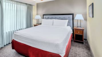 A hotel room with a large bed, two bedside tables with lamps, a ceiling fan, and a window with curtains.