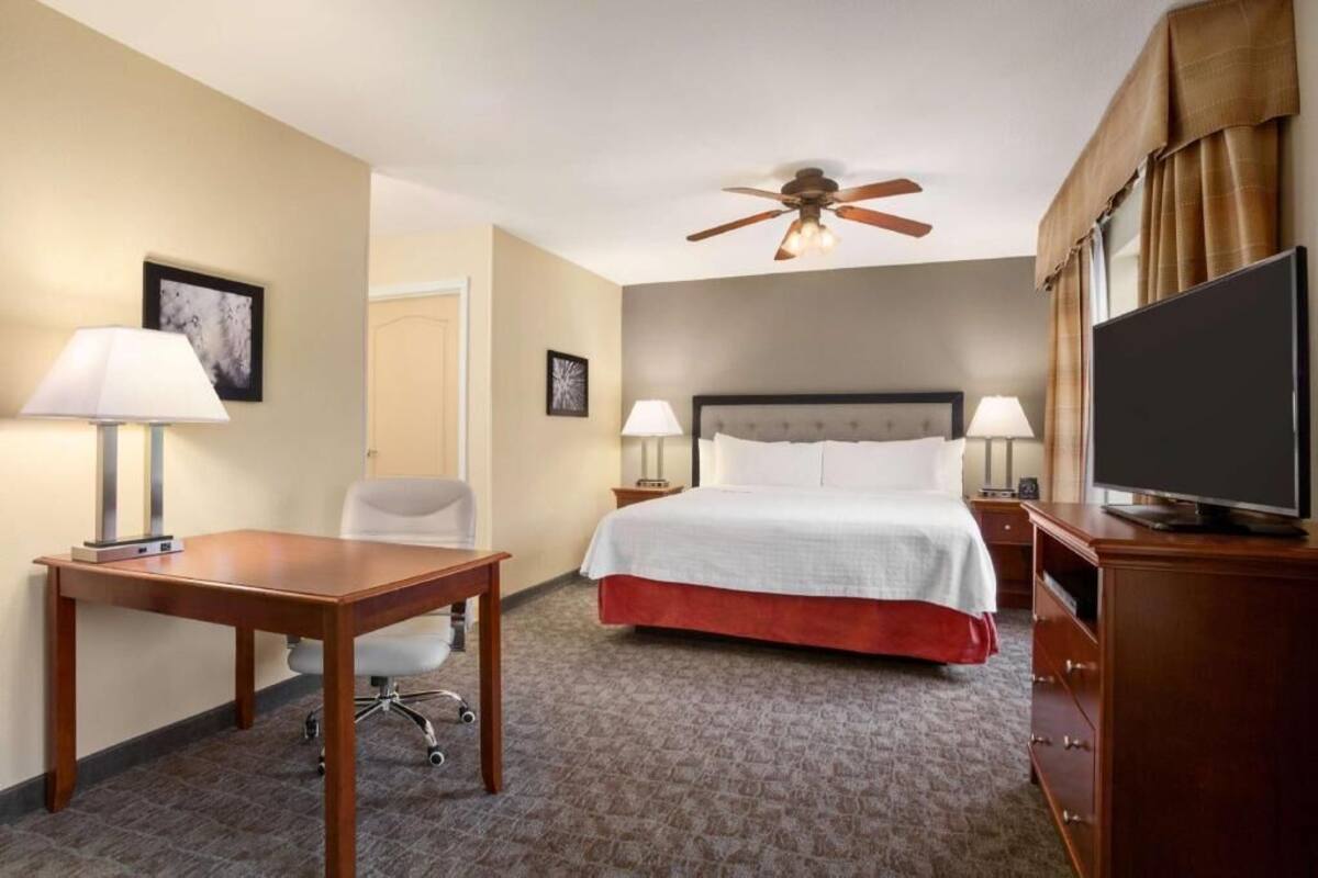 Une chambre d’hôtel équipée d’un lit, d’un bureau, d’une chaise, d’une télévision et d’un ventilateur de plafond.
