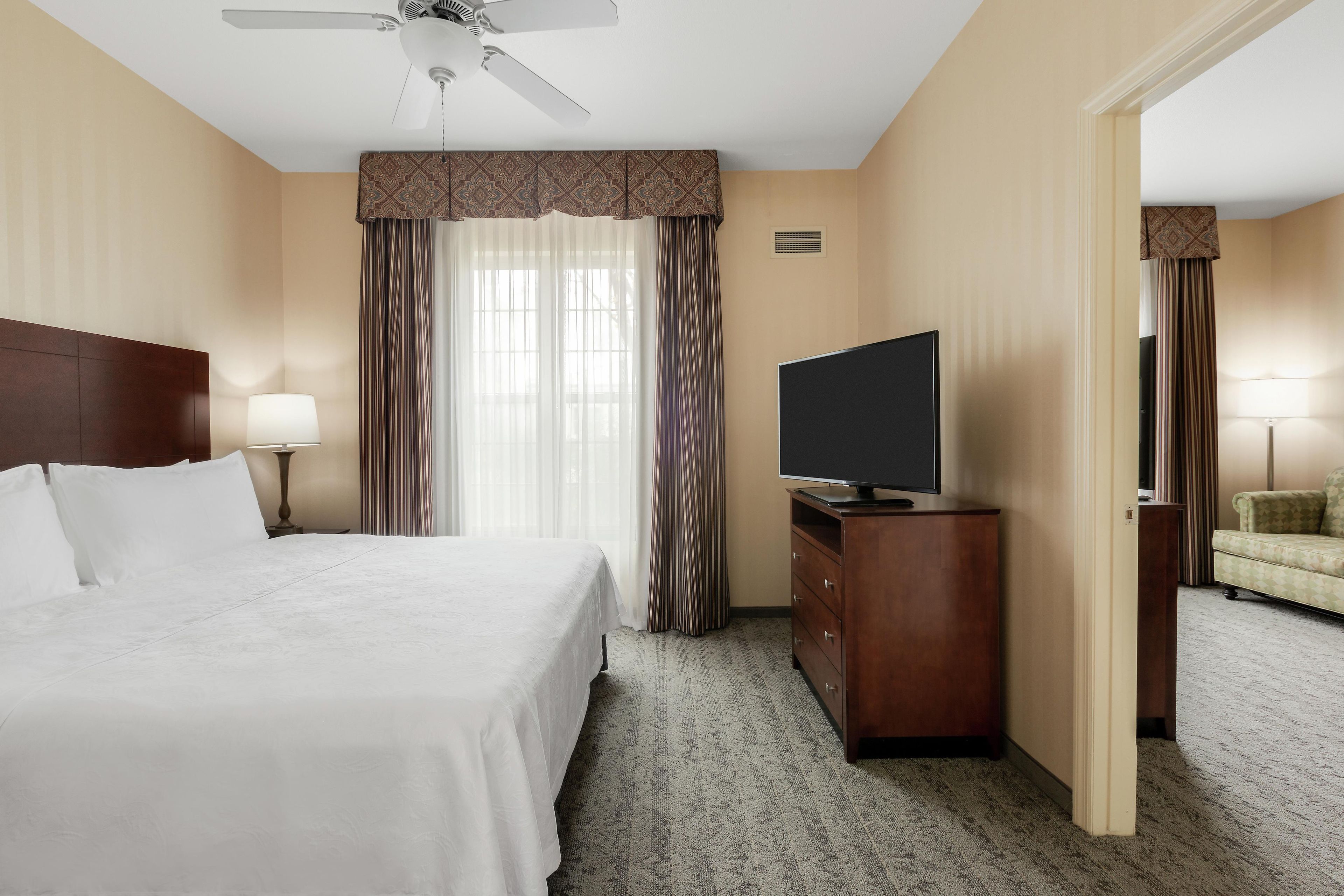 A hotel room with a bed, a television on a wooden dresser, a chair, and a ceiling fan.