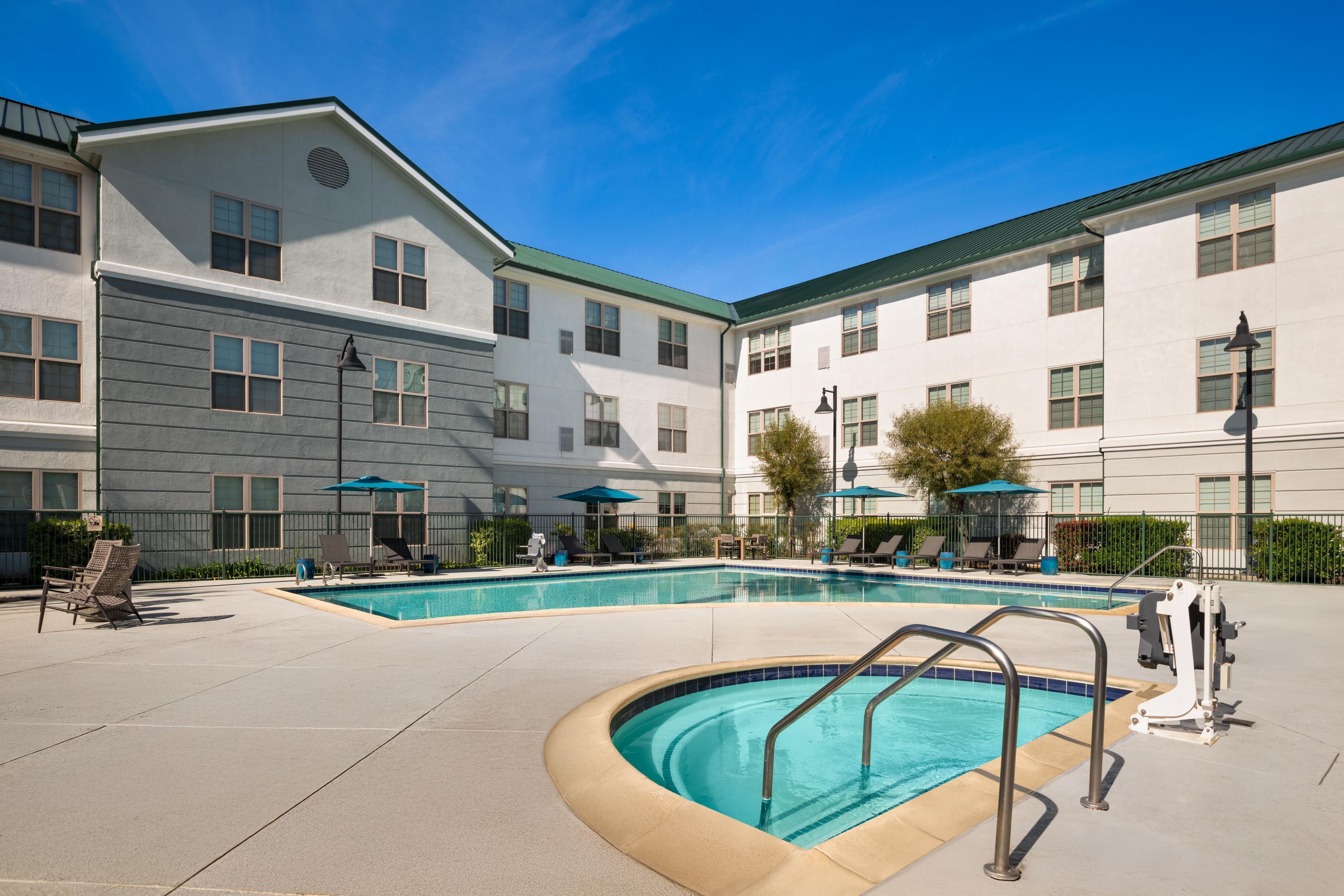 A hotel with a swimming pool, outdoor seating, and a covered patio area.