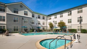 A hotel with a swimming pool, outdoor seating, and a covered patio area.