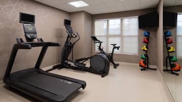 Sala de ginástica com esteira, elíptico, bicicleta ergométrica e um conjunto de bolas de exercício.