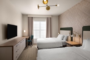 Ein Hotelzimmer mit zwei Betten, einem Schreibtisch, einem Sessel, einem Fernseher und einem Fenster mit Vorhängen.