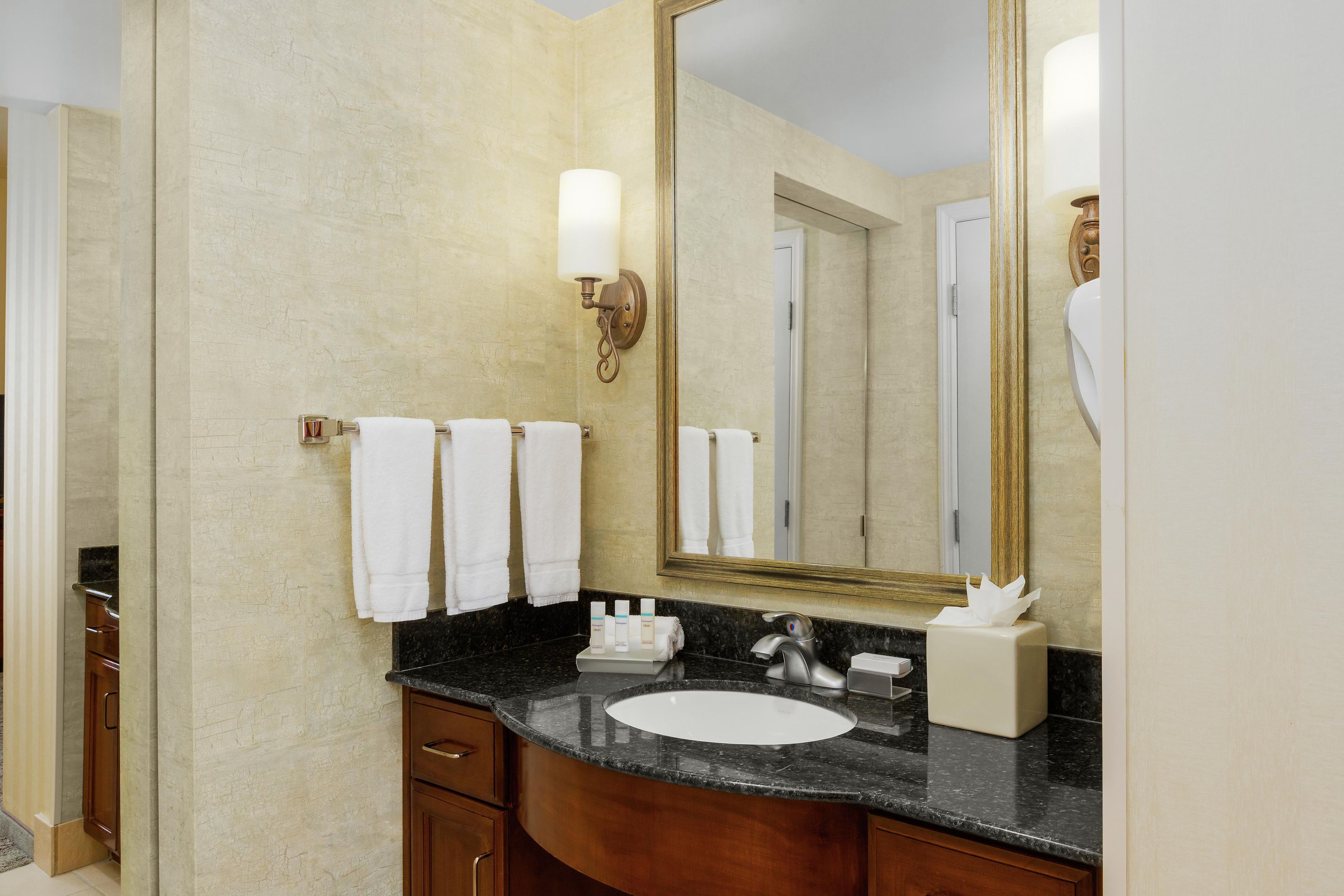 A bathroom with a marble sink, wooden cabinets, a large mirror, and two white towels hanging on the wall.