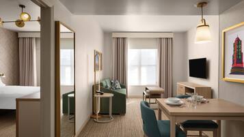 A hotel room with a bed, a sofa, a dining table with chairs, a TV, and a framed picture on the wall.
